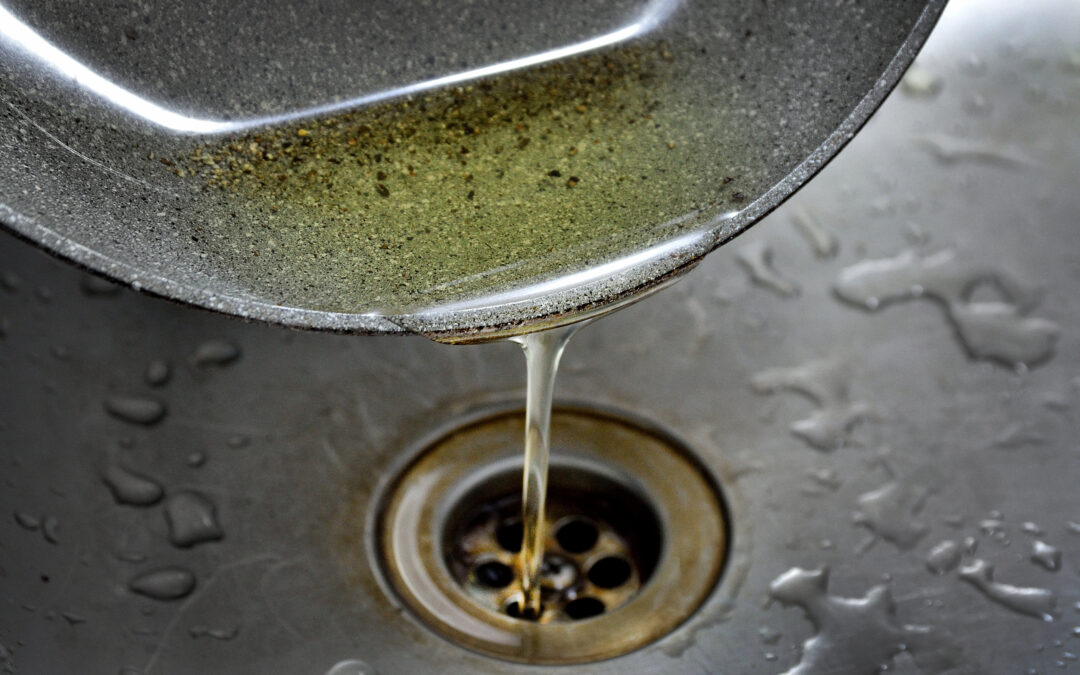 Oil from a frying pan being poured down a sink's plughole